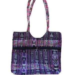 May include: A purple and black tote bag with a woven pattern and two zippered pockets. The bag has two handles with a pink and patterned design. The bag is made of a sturdy fabric and is suitable for carrying various items.