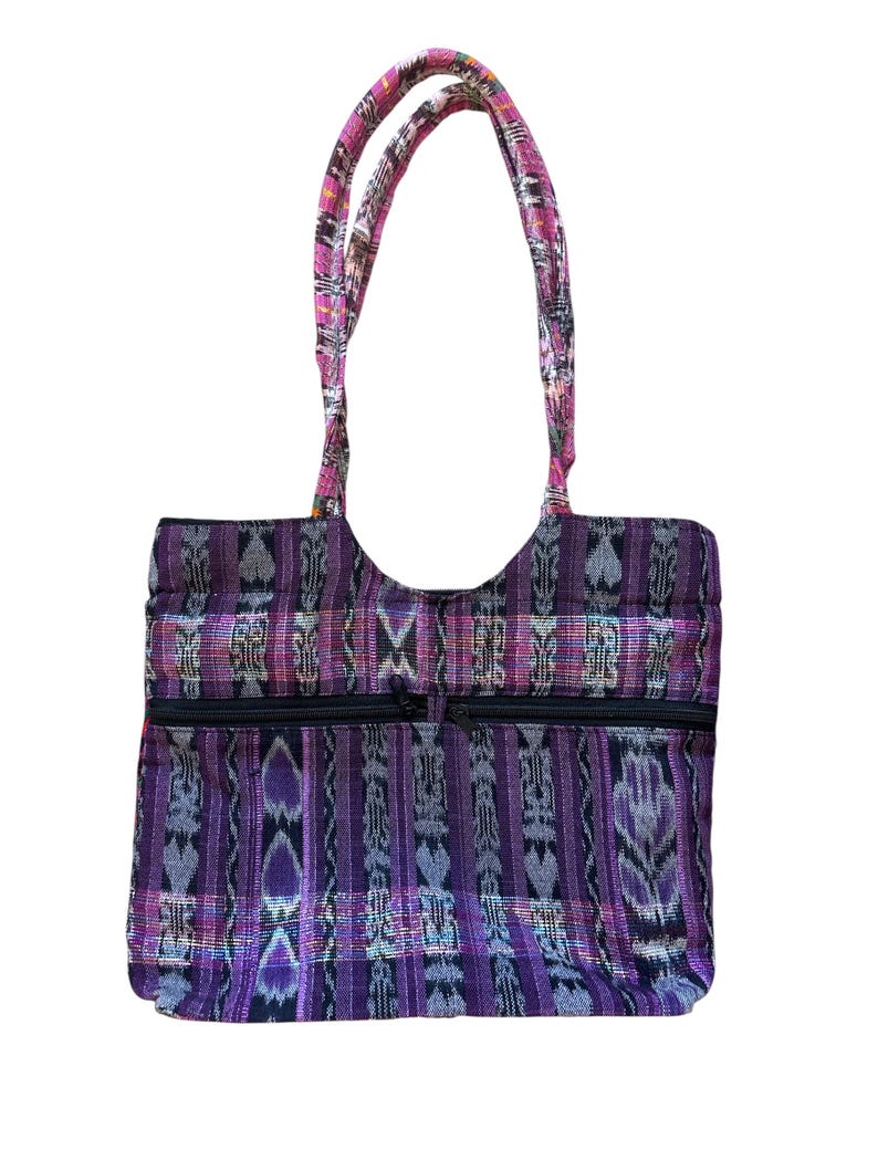 May include: A purple and black tote bag with a woven pattern and two zippered pockets. The bag has two handles with a pink and patterned design. The bag is made of a sturdy fabric and is suitable for carrying various items.