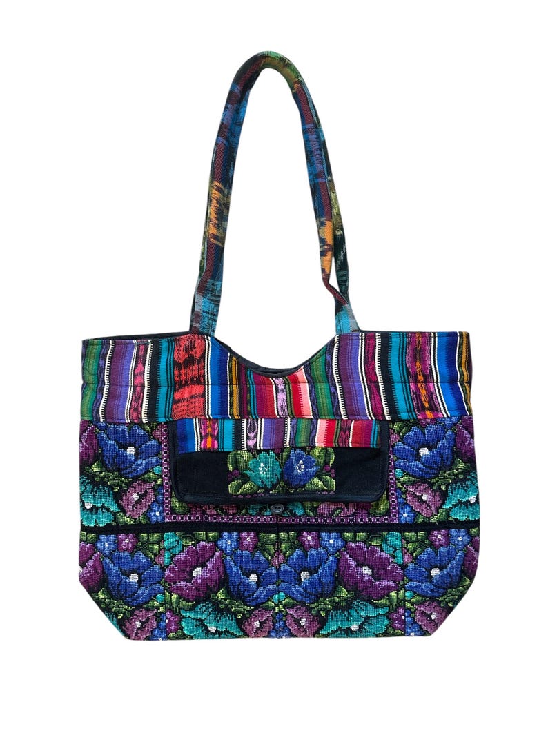 May include: A vibrant tote bag with a floral pattern. The bag has a black pocket with embroidered flowers and a striped top section. The handles are made of patterned fabric. The bag is approximately 38 cm wide and 36 cm tall.