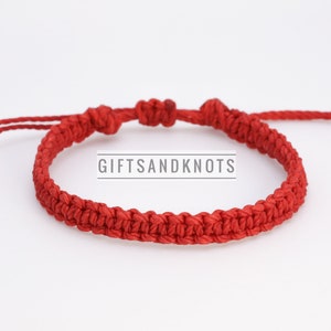 May include: A red braided friendship bracelet with a simple knot design. The bracelet is tied with a sliding knot for adjustability. The brand name "GIFTSANDKNOTS" is printed on a white background.