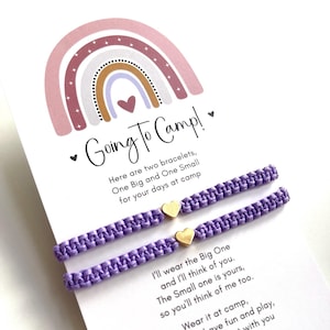 May include: Two lavender friendship bracelets with gold heart charms are displayed on a card with a rainbow and the words "Going To Camp!". The card includes a message about wearing the bracelets at camp.
