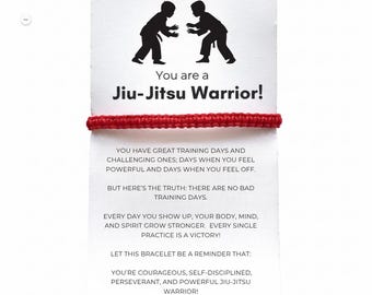May include: A red braided bracelet is displayed on a white card with the text "You are a Jiu-Jitsu Warrior!". The card features a black silhouette of two people practicing Jiu-Jitsu. The card also includes inspirational text.