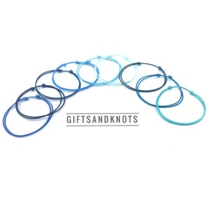 May include: A set of eight colorful string bracelets in shades of blue and teal. The bracelets are arranged in a semi-circle, with the text "GIFTSANDKNOTS" in the center.