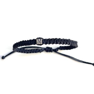 May include: A black braided bracelet with a silver charm featuring the letter "M".