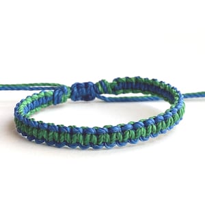 May include: A handmade macrame bracelet in shades of blue and green. The bracelet features a woven design with adjustable sliding knots for a comfortable fit. This accessory is perfect for adding a touch of color to any outfit.