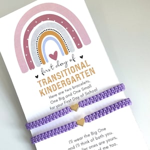 May include: A card with a rainbow design and the text "first day of TRANSITIONAL KINDERGARTEN" with two purple friendship bracelets with gold heart charms. The card says "Here are two bracelets, One Big and One Small for your First Day of School".