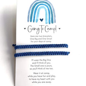 May include: Two blue woven cord bracelets attached to a white display card featuring a blue watercolor rainbow illustration and the text Going To Camp, along with a poem about wearing the bracelets while away at summer camp.