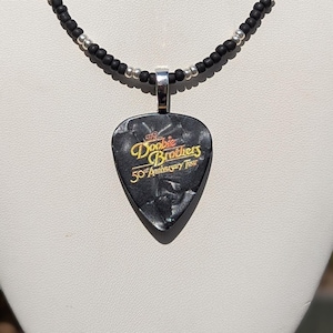 May include: Black and silver beaded necklace with a black guitar pick pendant that says "The Doobie Brothers 50th Anniversary Tour"