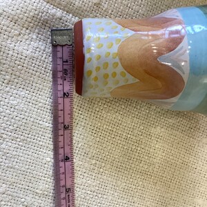 May include: A ceramic vase with a blue, orange, and yellow abstract design. The vase is approximately 6 inches tall.
