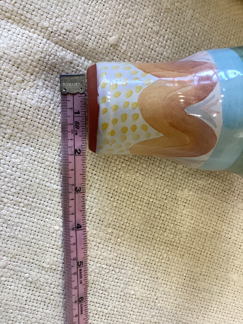 May include: A ceramic vase with a blue, orange, and yellow abstract design. The vase is approximately 6 inches tall.