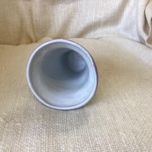 May include: A white ceramic vase with a light brown rim. The vase is empty and has a round opening at the top.