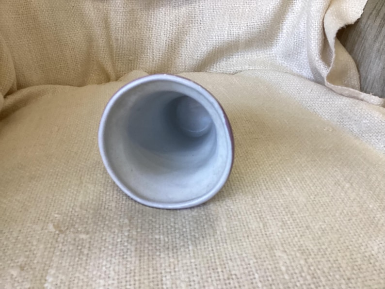 May include: A white ceramic vase with a light brown rim. The vase is empty and has a round opening at the top.