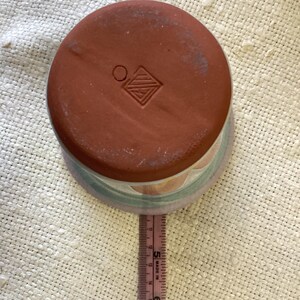 May include: A terracotta planter with a light blue, green, and orange design. The bottom of the planter has a stamped mark with a circle and a diamond shape.