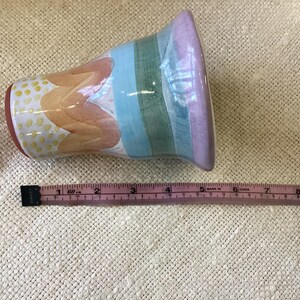 May include: A colorful ceramic vase with a striped design in shades of pink, blue, and green. The vase has a white background with a yellow and orange floral pattern.