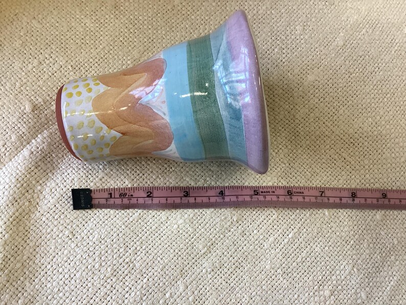 May include: A colorful ceramic vase with a striped design in shades of pink, blue, and green. The vase has a white background with a yellow and orange floral pattern.