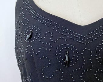 May include: A black sleeveless dress with a beaded pattern and two black crystal accents.