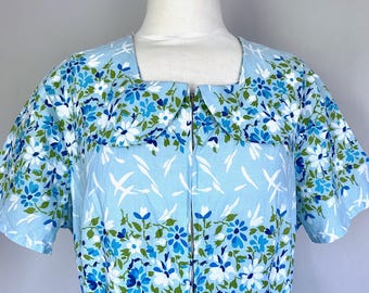 May include: A light blue vintage dress with a floral pattern. The dress features a square neckline, short sleeves, and a full-length zipper. The floral pattern includes blue, white, and green flowers and leaves. The dress is made of a lightweight fabric.