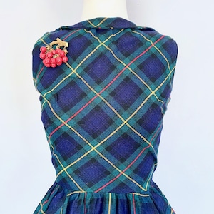 May include: A vintage plaid dress in shades of blue, green, and yellow, with a red and gold brooch. The brooch is shaped like a cluster of red berries. The dress has a collared neckline and a fitted bodice.