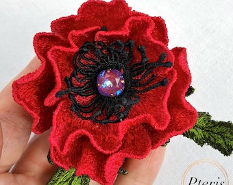 May include: A handmade red poppy flower brooch with black detailing and an iridescent gem at its centre. The brooch has detailed embroidery and green leaves, ideal for adding a floral accent to any outfit.