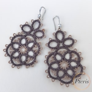 May include: A pair of brown and beige crocheted earrings with a delicate, intricate design. The earrings are made of a fine thread and have a silver hook.