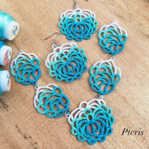May include: A set of teal and white crocheted earrings with a delicate, lacy design. The earrings are made with a gradient of colors, starting with white and transitioning to teal. The earrings are hanging from silver hooks.