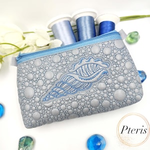 May include: A gray zippered pouch with a textured, bubble-like pattern and a blue seashell embroidery. The pouch has a blue zipper and is filled with blue thread spools. The design is reminiscent of the ocean.