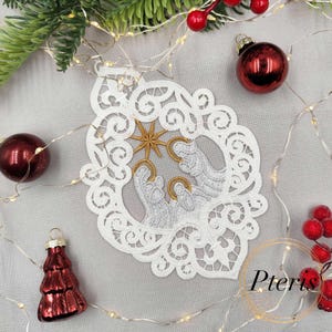 May include: A white lace Christmas ornament with a Nativity scene, featuring Mary, Joseph, and baby Jesus, and a gold star. The ornament is surrounded by red Christmas balls, a red tree ornament, and string lights.