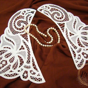 Può includere: Un paio di colletti in pizzo bianco con intricati motivi floreali e geometrici, accompagnati da una singola collana di perle color crema. Il testo Pteris è visibile nell'angolo in basso a destra dell'immagine.