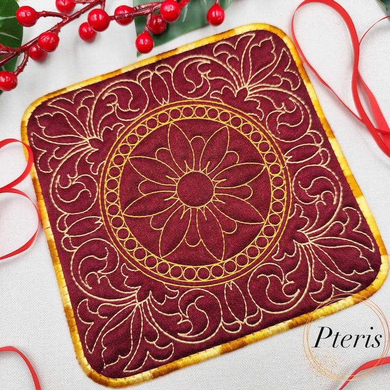 May include: A square, burgundy-colored coaster with a gold embroidered floral design. The coaster has a gold border and a central circular floral pattern. The design is intricate and detailed, with a vintage aesthetic.