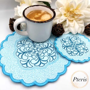 Könnte beinhalten: Eine weiße Emaille-Tasse mit Kaffee steht auf einem hellblauen Untersetzer-Set. Die Untersetzer haben einen gewellten Rand und ein detailliertes blaues Blumendesign. Weiße Blumen und braune gewebte Kugeln sind ebenfalls vorhanden.