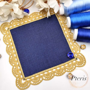 Może przedstawiać: Kwadratowy granatowy materiał z złotą szydełkową obwódką i wykończeniem. Obramowanie ma falisty brzeg. Niebieskie szpulki nici i dekoracyjne niebieskie i złote klejnoty znajdują się w tle. Słowo "Pteris" znajduje się w prawym dolnym rogu.