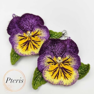 May include: Embroidered pansy earrings with purple petals, yellow and gold centres, and green leaves. The earrings have silver-coloured findings. The earrings are a floral theme.