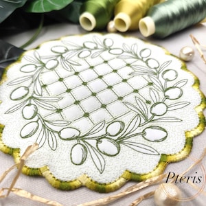 Puede incluir: Posavasos blanco bordado con un diseño de rama de olivo verde. El posavasos tiene un borde festoneado con ribete verde y dorado. El centro presenta un patrón de cuadrícula con costuras verdes. Hilos decorativos y perlas en el fondo.