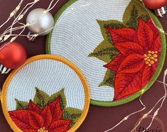 Peut inclure: Deux dessous de verre brodés circulaires présentant un motif de poinsettia rouge et vert sur fond blanc. Le plus grand a une bordure verte, le plus petit une bordure dorée. Ils sont entourés de guirlandes lumineuses et de boules.