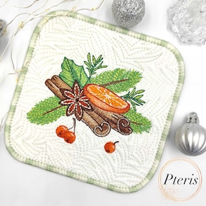 May include: Embroidered square trivet with a festive design. Features cinnamon sticks, star anise, orange slice, and greenery. The trivet has a white background with a green border and a quilted pattern. Decorative Christmas-themed kitchenware.