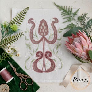 Op de afbeelding: Een wit stoffen paneel met een ingewikkeld geborduurd botanisch ontwerp in mauve en saliegroen. Het borduurwerk toont een centraal dennenappelachtig motief met symmetrische krullende stelen. De tekst Pteris is in het zwart gedrukt.