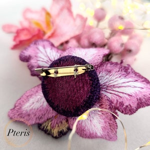 Puede incluir: Un broche de flor bordada en color morado y rosa con cierre de pin. El broche est&aacute; hecho de terciopelo y sat&eacute;n.