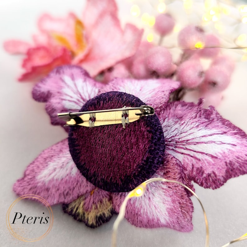 Puede incluir: Un broche de flor bordada en color morado y rosa con cierre de pin. El broche est&aacute; hecho de terciopelo y sat&eacute;n.