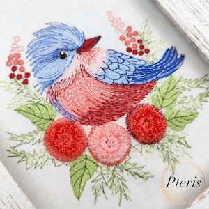 Könnte beinhalten: Eine gestickte Darstellung eines blauen und roten Vogels mit einem flauschigen blauen Kopf, der auf einem Bett aus grünen Blättern und roten und rosa Blüten sitzt. Das Design ist auf einen weißen Stoffhintergrund gestickt.