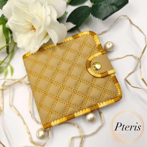 May include: Tan quilted wallet with gold trim and a gold snap closure. The wallet has a diamond pattern and is surrounded by white flowers and pearls. The word "Pteris" is in the lower right corner.