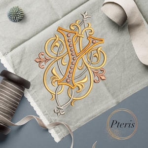 May include: Embroidered letter Y in gold with ornate silver and copper scrollwork on a light gray linen fabric. The letter is surrounded by a gold circle with the word "Pteris" in gold lettering.