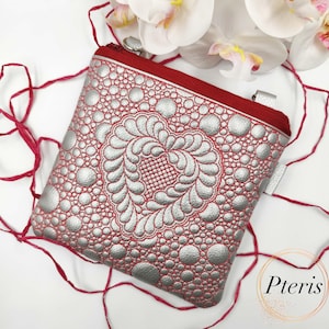 May include: A square, silver and red zippered pouch with a heart-shaped design. The pouch features a silver, textured pattern of circles and a red zipper and trim. The design includes a heart-shaped pattern in the center.
