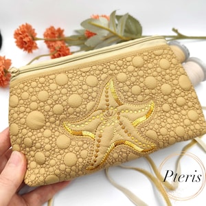 May include: Tan zippered pouch with a quilted pattern and a gold embroidered starfish design. The pouch has a beige zipper and the word "Pteris" in a gold circle.