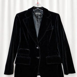 Peut inclure: Un blazer en velours noir doté d'un revers cranté, de deux boutons sur le devant et de deux poches à rabat de chaque côté. La veste comprend une doublure intérieure noire et une étiquette au col avec le texte CHAUS. Vêtement sur cintre.