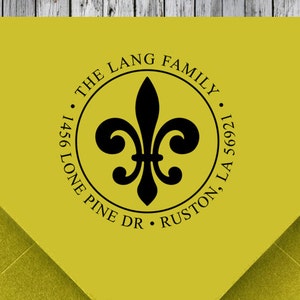 K&ouml;nnte beinhalten: Ein gelber R&uuml;cksendeaufkleber mit einem schwarzen Fleur-de-lis-Design. Der Text lautet "The Lang Family, 1456 Lone Pine Dr, Ruston, LA 56921."