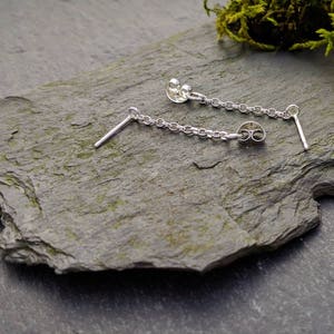 May include: A pair of silver chain earrings with a small, round charm at the end of each chain.