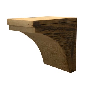 May include: A wooden corbel with a dark brown, textured finish. The corbel has a curved, arched support and a flat top, ideal for supporting shelves or architectural elements. The wood grain is visible throughout the piece.