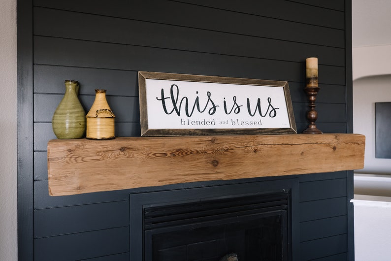 May include: A wooden mantel with a framed sign that reads "This is us, blended and blessed". There are two decorative vases and a candle holder on the mantel.