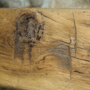 May include: Close-up of a weathered wooden beam with knots and cracks. The wood is a light brown color with darker brown streaks.