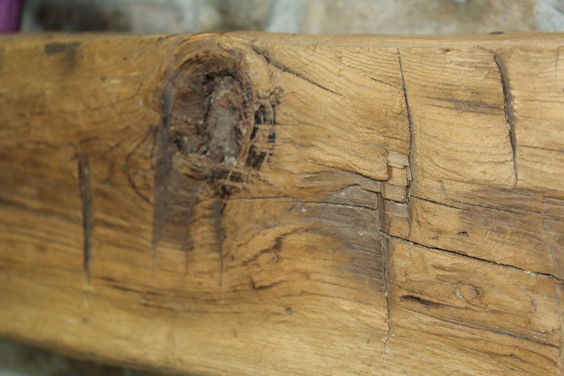 May include: Close-up of a weathered wooden beam with knots and cracks. The wood is a light brown color with darker brown streaks.